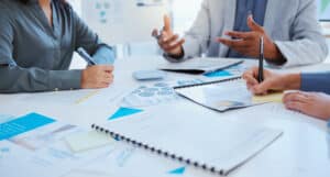Business professionals discussing proposed charts and data at a conference table with laptops and documents visible.