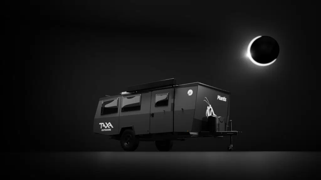 A black camper trailer with Auto Draft white branding parked under a dim light against a dark background.