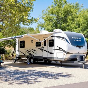 A modern RV parked on a well-maintained gravel pad surrounded by light desert vegetation under a clear blue sky, highlighting the serene camping environment.