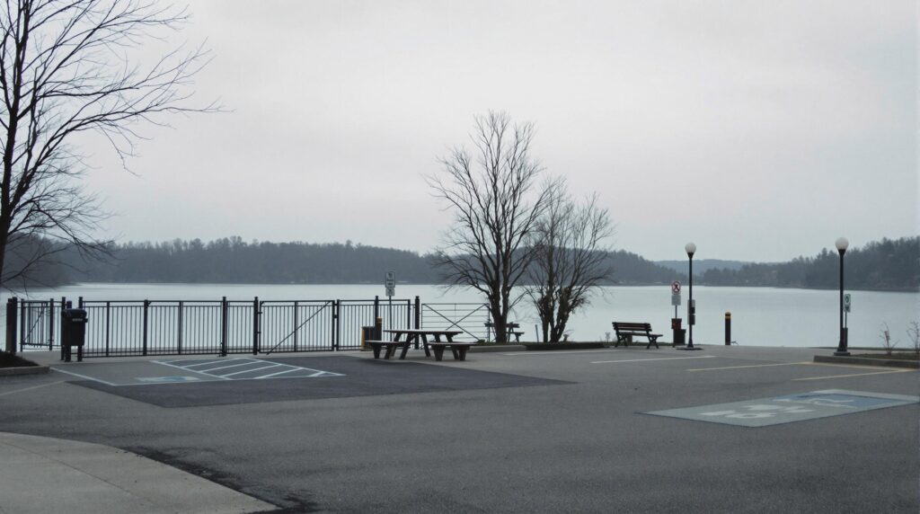 Deserted lakeside recreation area with a closed gate, empty parking lot, and overcast sky.