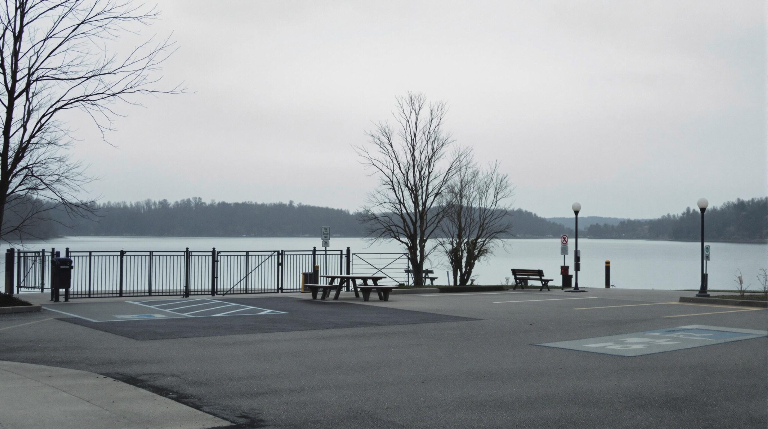 Deserted lakeside recreation area with a closed gate, empty parking lot, and overcast sky.