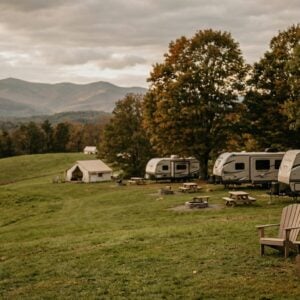 Canvas glamping tents and travel trailers lined up on a grassy hill at Green Mountain Retreat, with wooden Adirondack chairs and picnic tables overlooking a scenic mountain valley during autumn