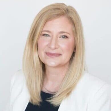 A woman in a white blazer and black top, engaging in MC Fireside Chats.