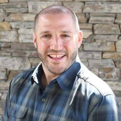 MC Fireside Chats: A man in a plaid shirt smiling in front of a stone wall.