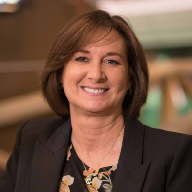 A smiling woman in a black jacket and floral shirt participates in MC Fireside Chats.